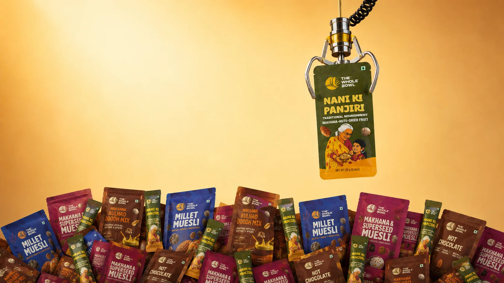A claw machine lifting a Nani Ki Panjiri sachet above a pile of The Whole Bowl packs